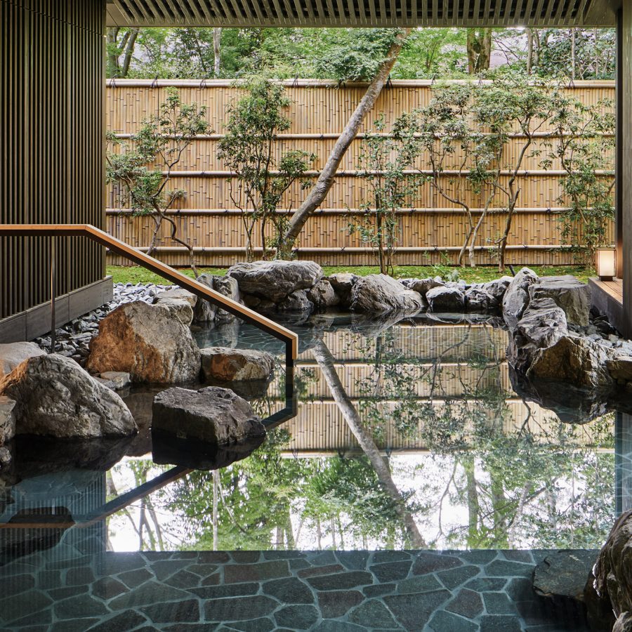 An onsen pool framed by rocks with a garden behind it.