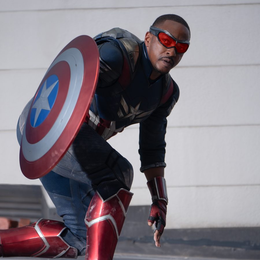 In a scene from Captain America: Brave New World, hero Sam Wilson (Anthony Mackie) crouches on the ground, holding the Captain America red white and bule shield. 