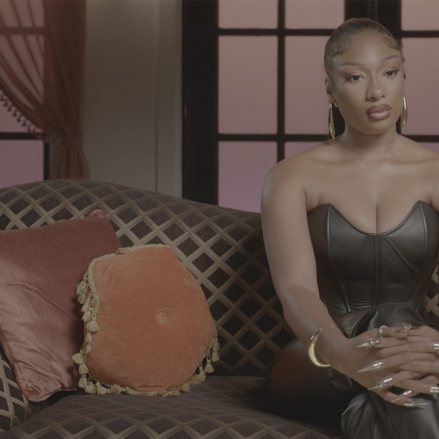 In an interview scene from Megan Thee Stallion: In Her Words, rapper Megan Thee Stallion sits on a sofa in a pink-hued room. 