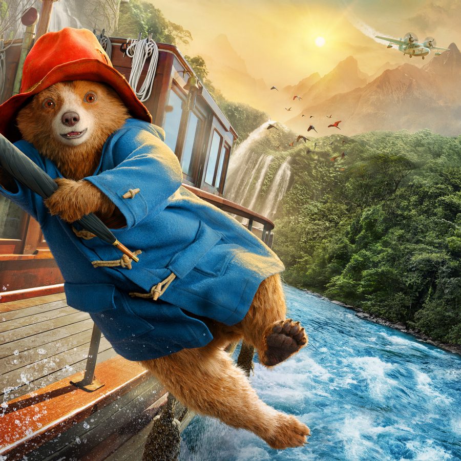 In a scene from CGI live action film Paddington in Peru, Paddington the bear swings from a boat on a rainforest river. He wears his signature blue coat and red hat. 