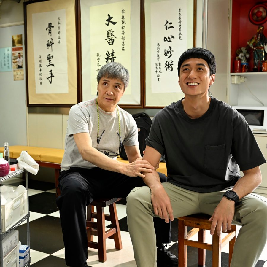 In a scene from Stuntman, older stuntman trainer Sam (Stephen Tung Wai) and aspiring stuntman Long (Terrance Lau) sit on stools in an apartment. 
