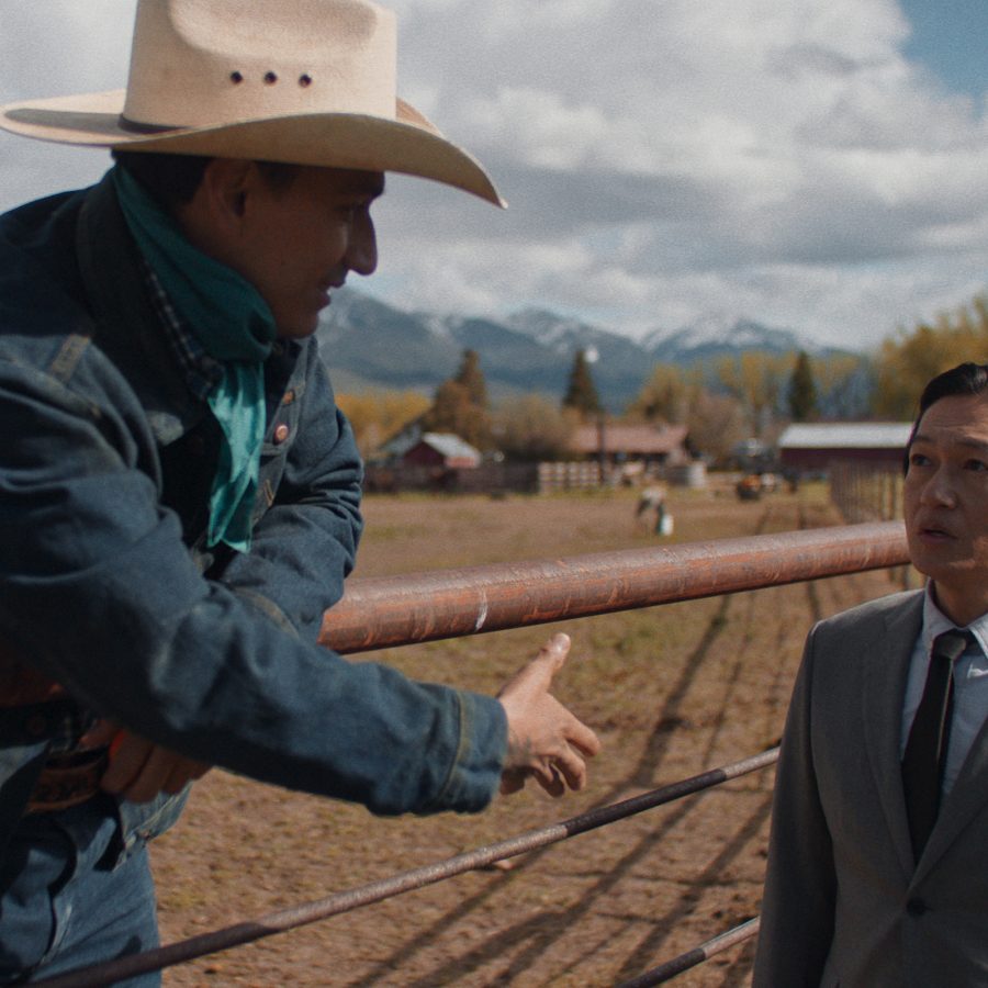 In a scene from Tokyo Cowboy, two men stand on a cattle ranch. One is dressed in cowboy attire. The other – protagonist Hideki (Arata Iura) – wears a suit. 
