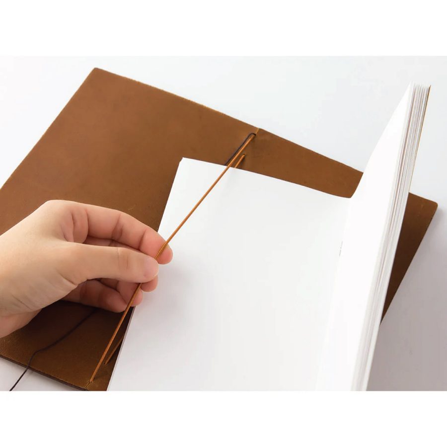 Person adding a new sheave of pages to a Traveler’s notebook.