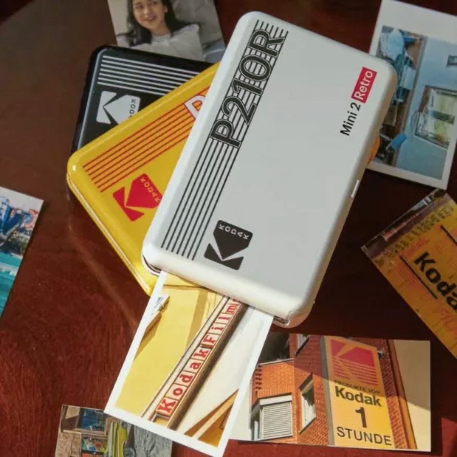 A Kodak P210RW Mini2 Retro 4PASS photo printer printing a picture with photos strewn around it.