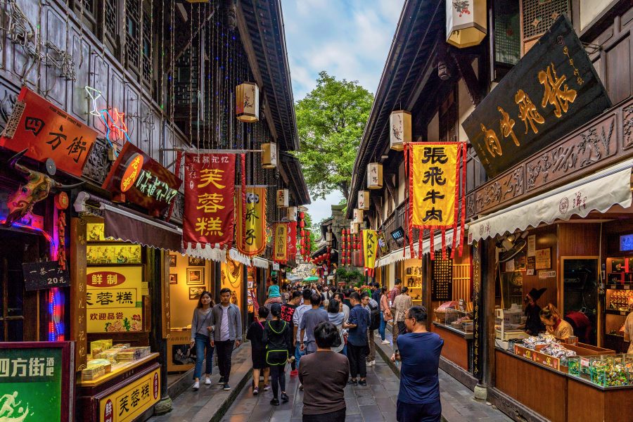 People walking down Jinli Ancient Street with various shops, signs, and old buildings. 