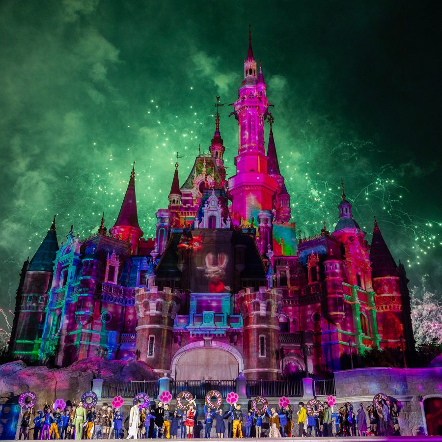 Exterior view of the iconic castle at Shanghai Disneyland at night, with the sky lit up by fireworks.