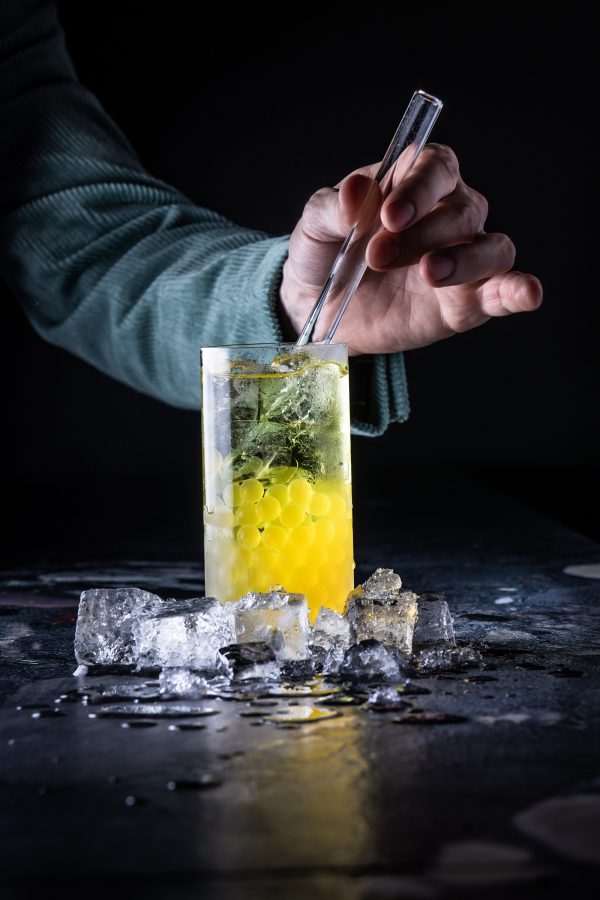 A person mixes a cocktail filled with yellow pearls, available at Confessions in Brussels. 