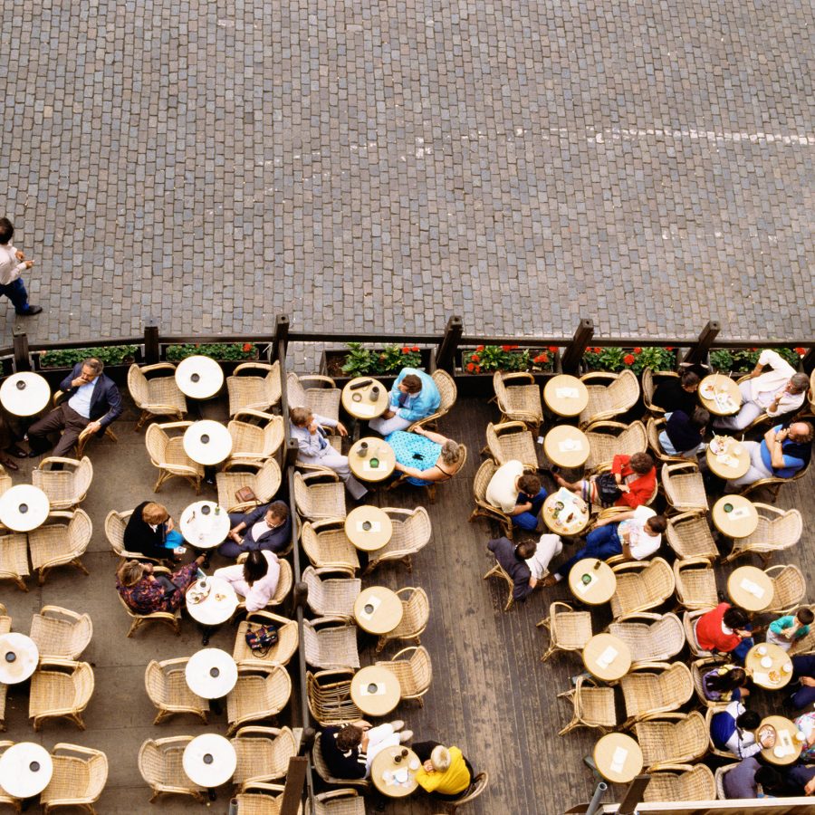 A top-down view of outdoor seating at a Brussels eatery shows a pedestrian walking next to multiple dining tables. 