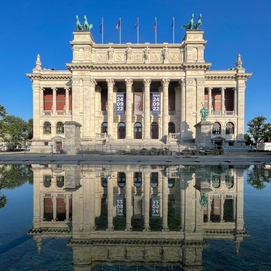 The exterior of The Royal Museum of Fine Arts in Brussels features a portico with flags lining the top.