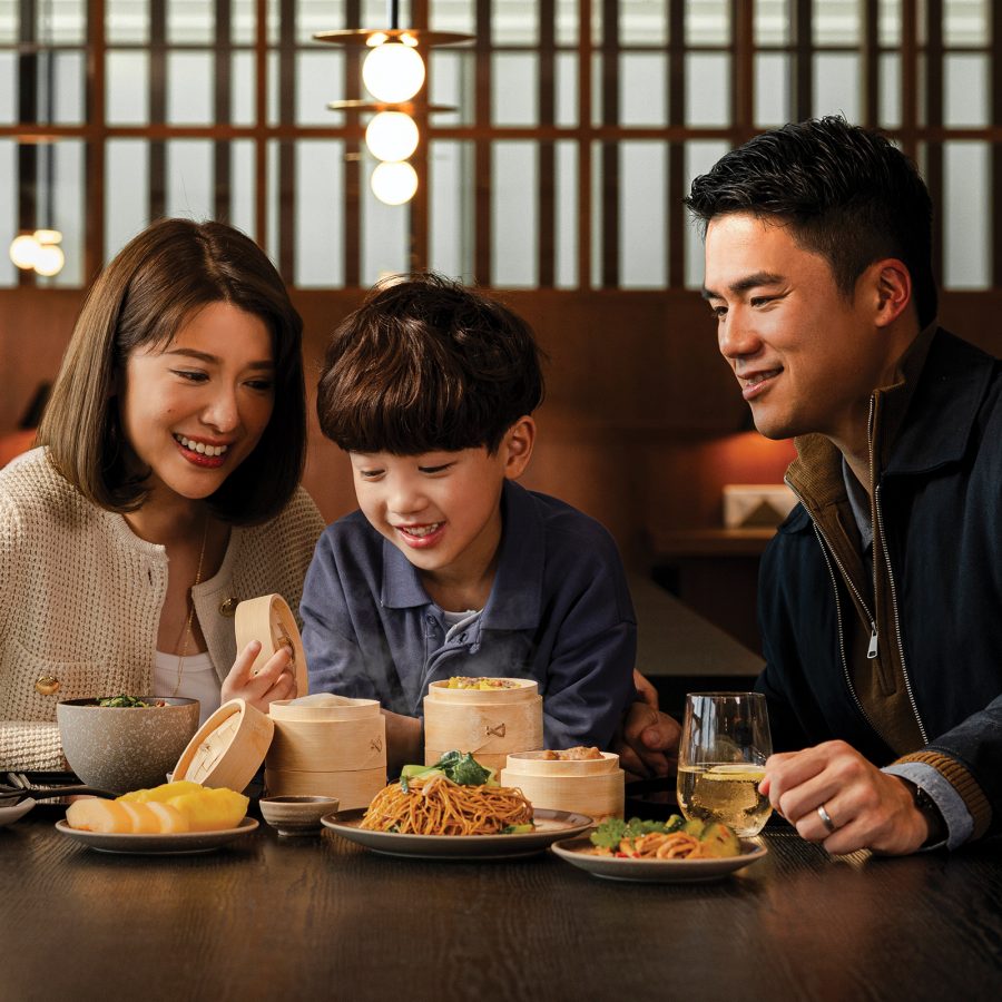 A family of three gather around mini dim sum steamers and plates of Chinese food at The Bridge. 