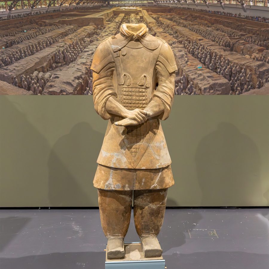 A Terracotta Warrior without a head stands in front of a wall at the WA Museum