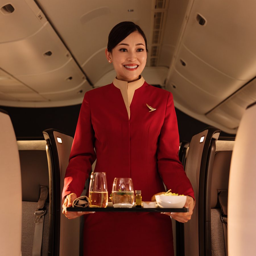 A Cathay Pacific cabin crew member smiles while carrying a meal tray in the cabin. 