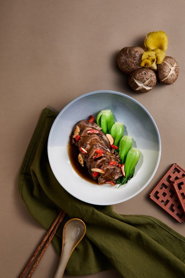 Top-down view of Minnan braised herbal beef served with Shanghai bok choy. Mushrooms, chopsticks and decorative coasters are placed around the dish.