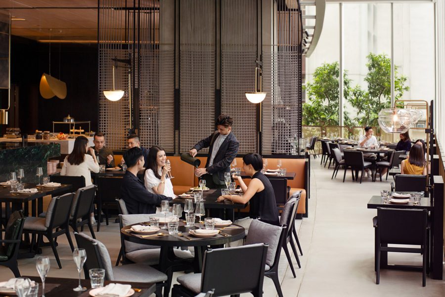 people dining inside the restaurant of FEAST at East Hotel during daytime while a server pours a drink into a glass