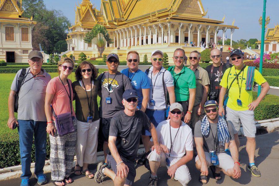 A group of LGBT+ travellers smile as they pose in front of a Thai temple.