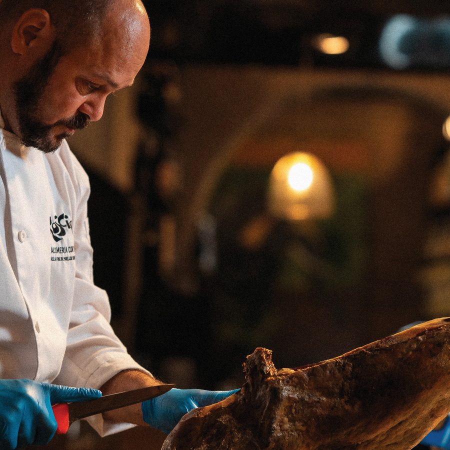 Italian chef carving a leg of ham with a small knife at Roscioli in Rome.