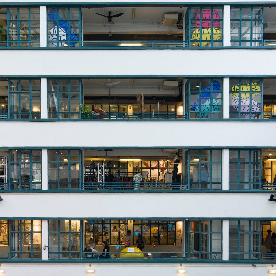 Multiple storeys of PMQ consist of long hallways bordered by green framed windows. 