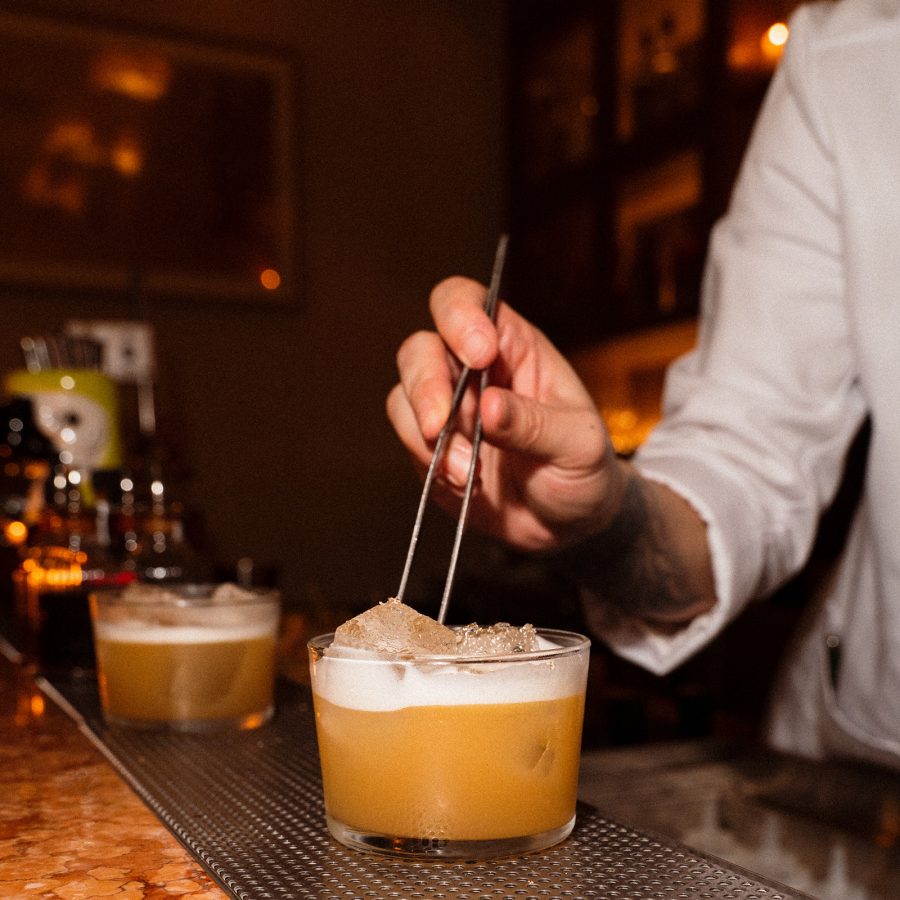 A mixologist puts ice inside an orange drink. 