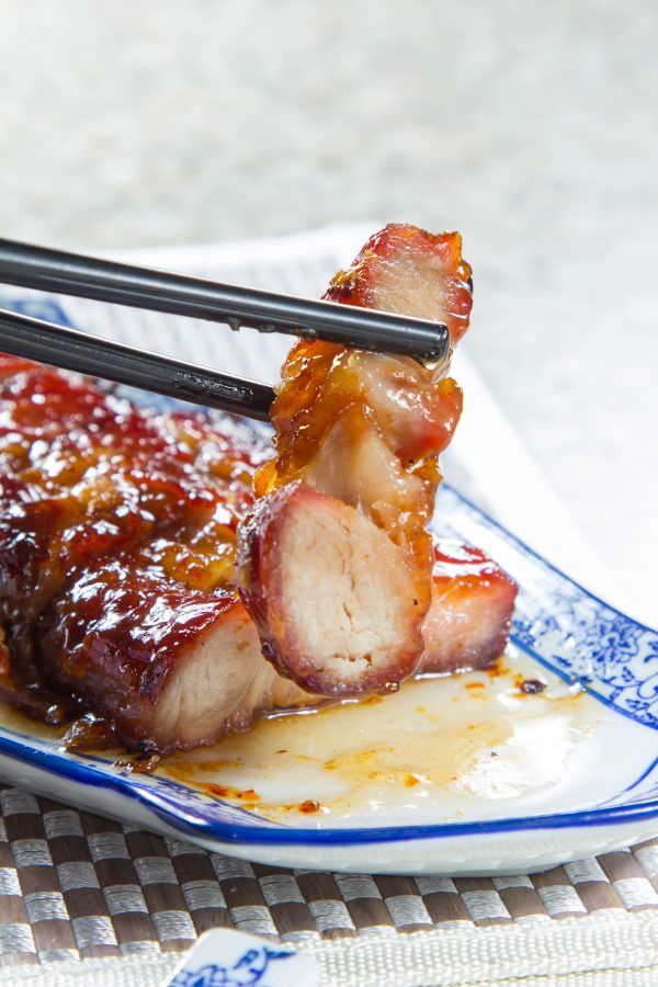 Chopsticks pick up a piece of char siu. 