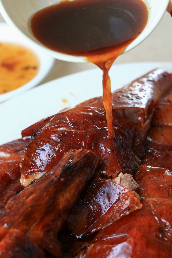 A person pours sauce over a plate of roast goose. 