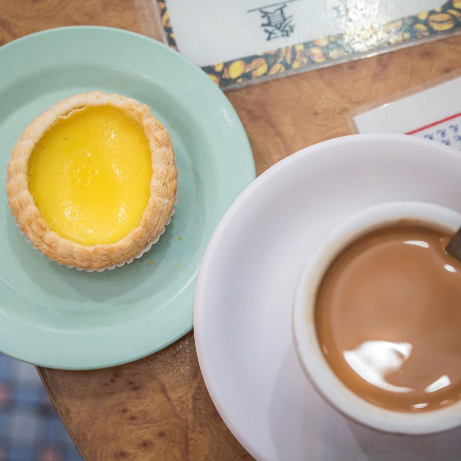 An egg tart is placed next to a cup of milk tea.