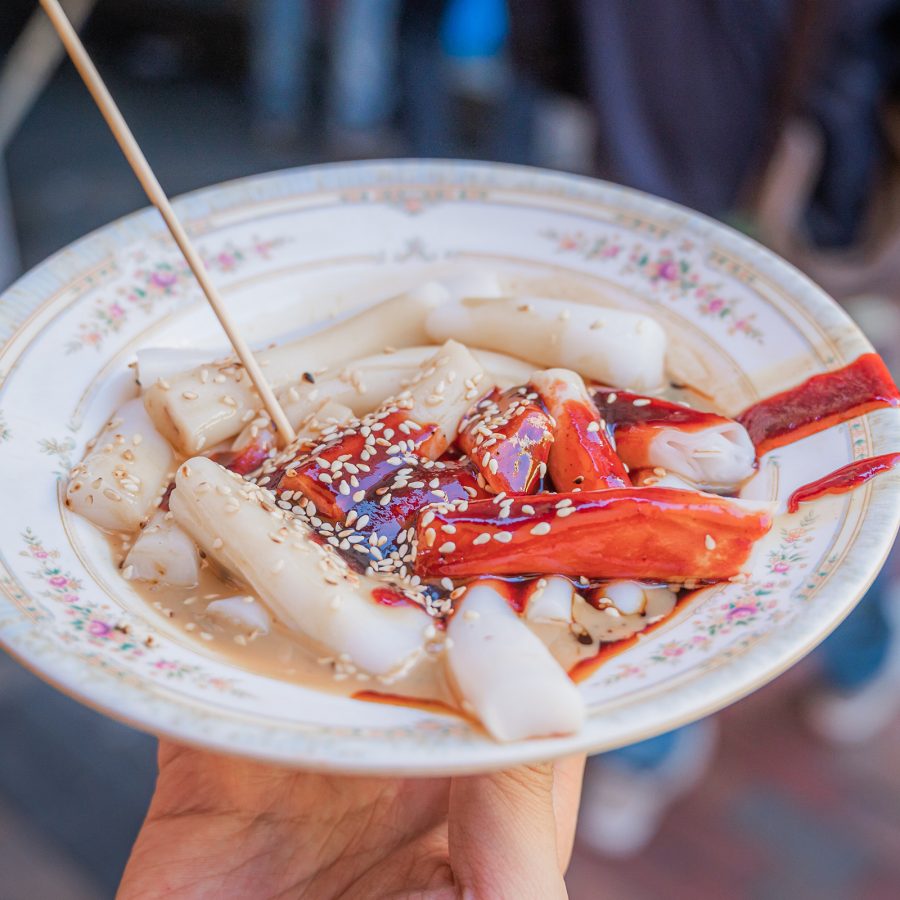 A person holds a plate of cheung fun covered with sauce. 