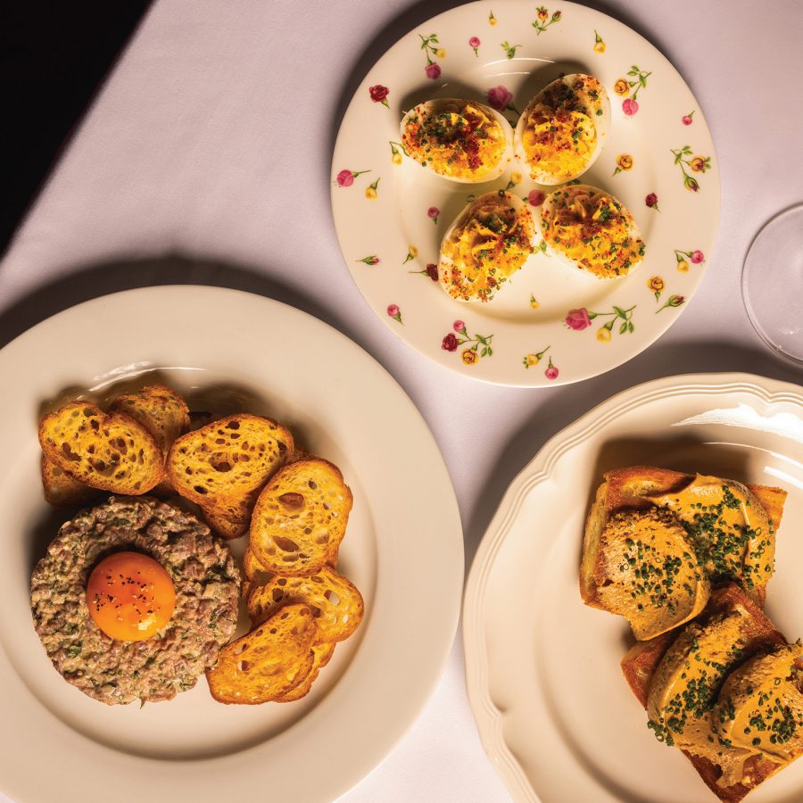 Plates of food and a glass of wine are arranged across a table at Jean-Pierre.
