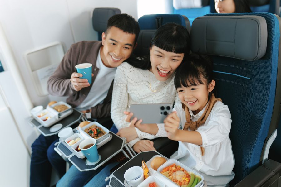 A young girl holds up her phone for a selfie with her parents on a plane.