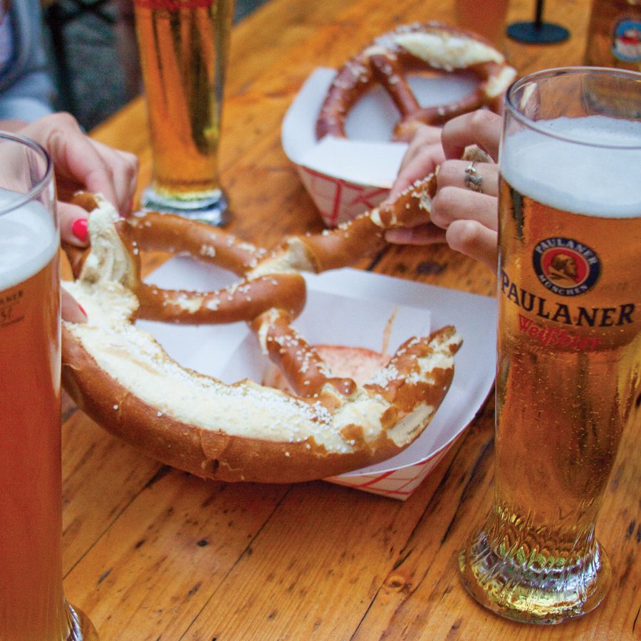 A view of two people’s hands as they enjoy a pretzel and beers