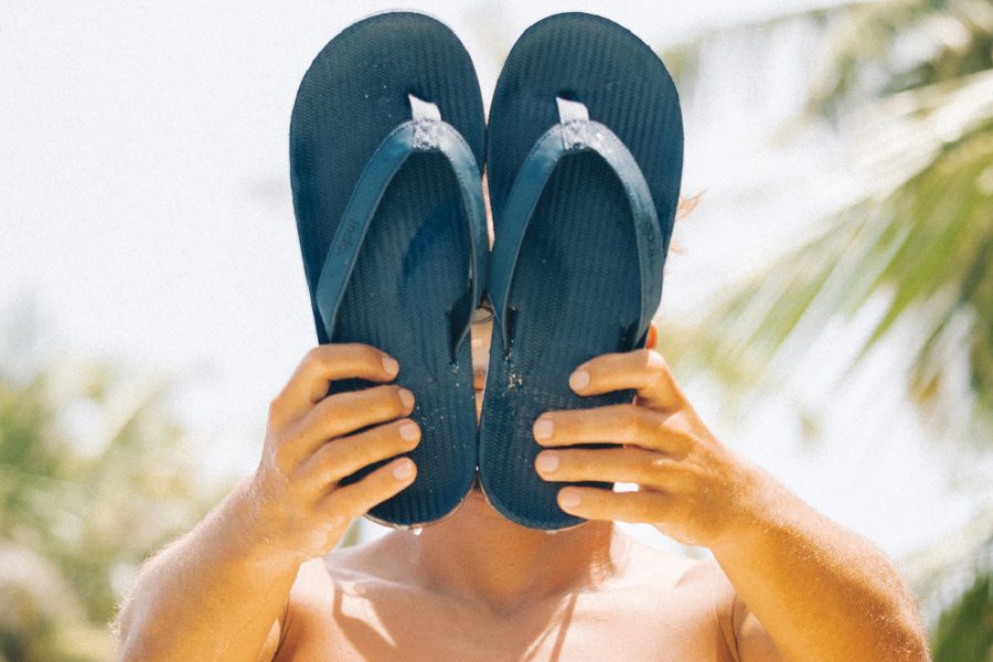 A person holds up a pair of teal flip flops in front of their face outdoors.