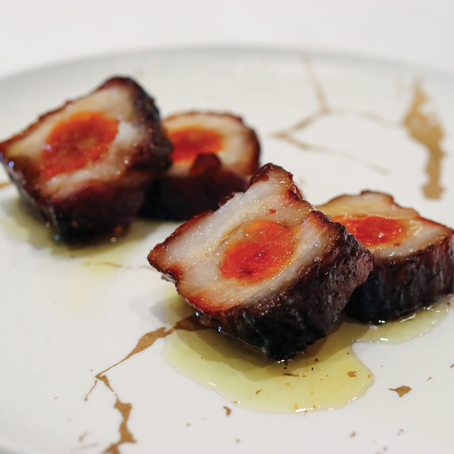  Close-up view of someone using chopsticks to pick up steamed rice rolls covered in soy sauce.