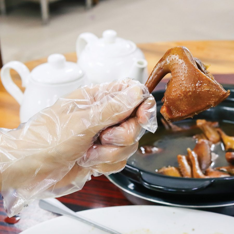 A diner wearing a plastic glove holding a braised pigeon leg 