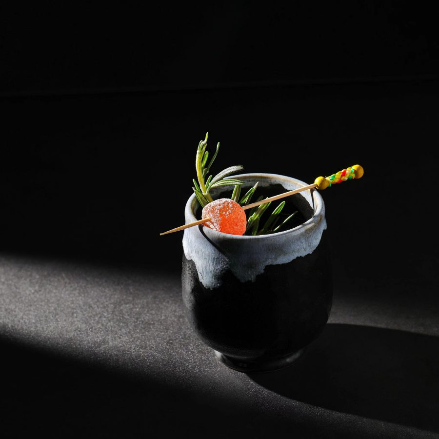 A moody shot of a cocktail in a black and grey ceramic cup with sugar candy garnish on a toothpick, served at The Union Trading Company bar, Shanghai.