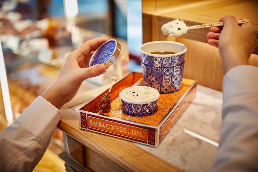A person raises a spoon filled with ice cream over a blue cup on a Bacha Coffee Room tray.