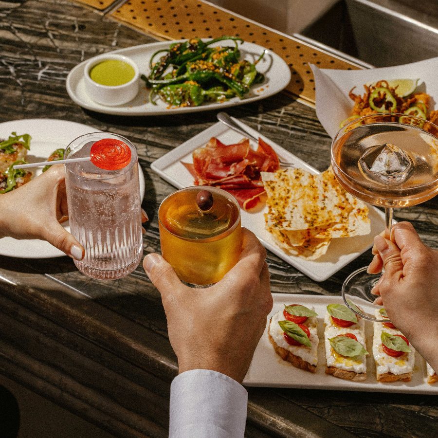 People raise three cocktails of a plate of dishes at La Petite Maison in Hong Kong.
