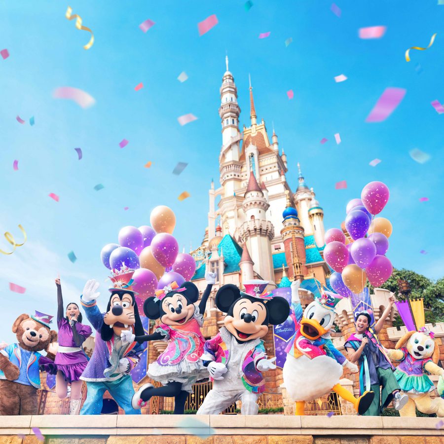 Mickey Mouse and friends raise their arms in the air in front of Hong Kong Disneyland castle as confetti streams.