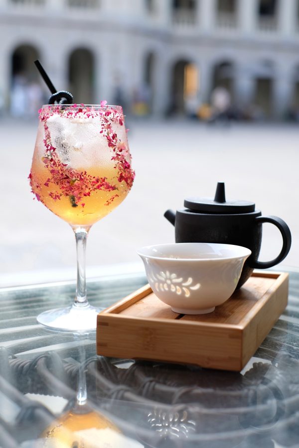 A close up of a tea cocktail and Chinese tea pot and cup with a view of the outdoor courtyard at LockCha Tea House in Tai Kwun.
