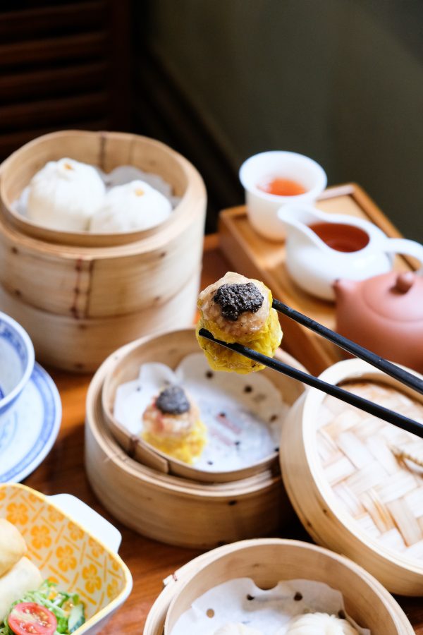 A close up of a chopsticks holding a vegetarian shao mai over baskets of dum sum and Chinese tea served at LockCha Tea House.