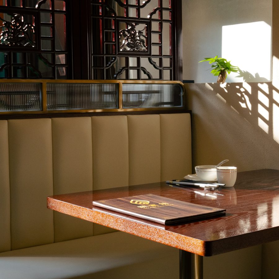 A view of a dining table with booth seating at Veggie Kingdom with natural sunlight spilling through a Chinese design wall partition. 