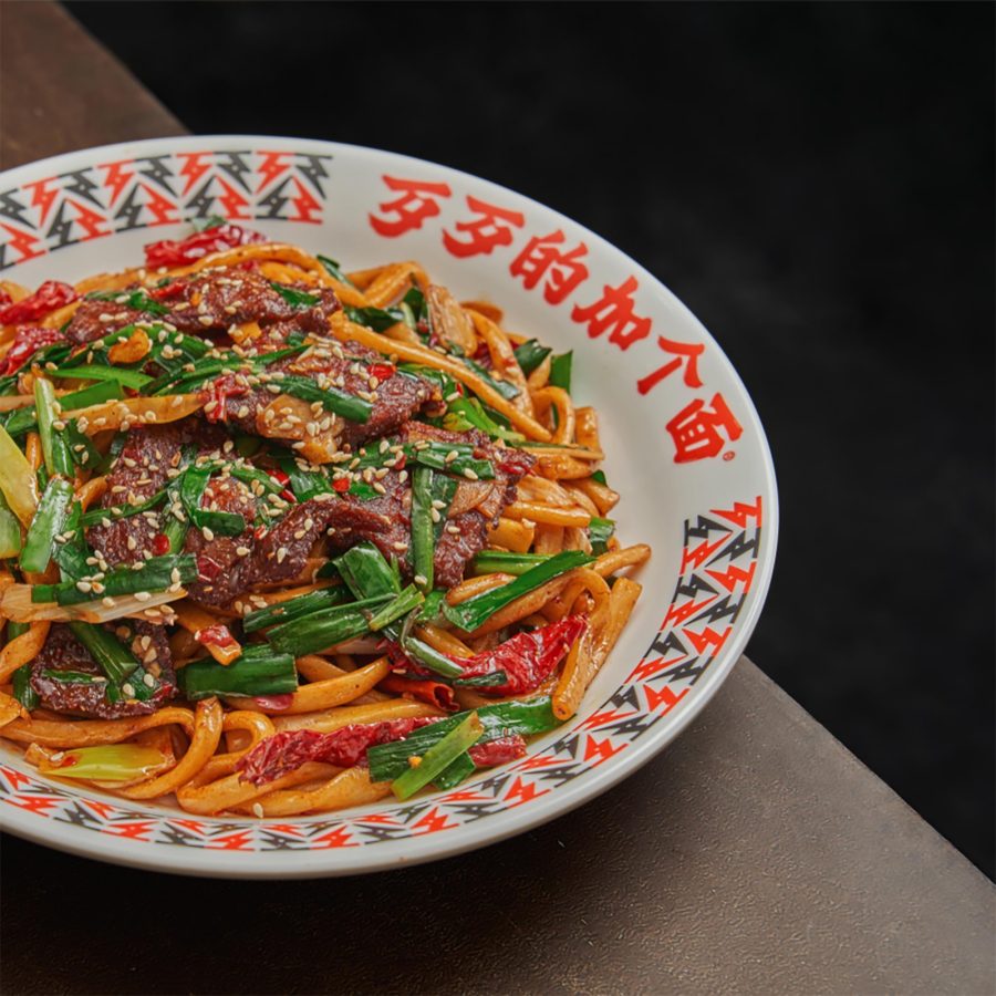 A bowl of laghman noodles on a table features stir-fried ingredients. 