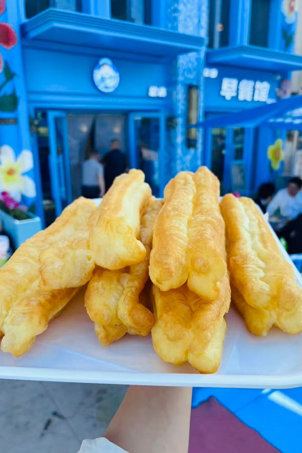 A person holds up a plate of fried dough outside a restaurant.