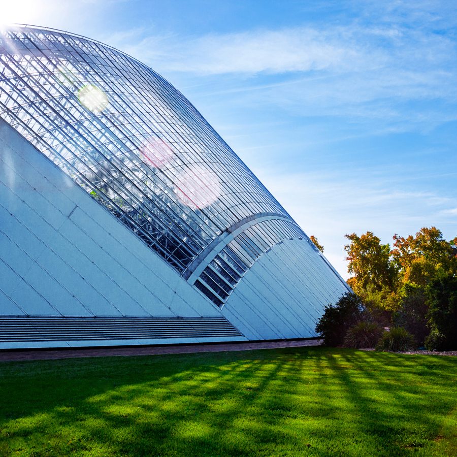 Sun shines on the curved glass roof of Adelaide Botanic Garden on a blue day.