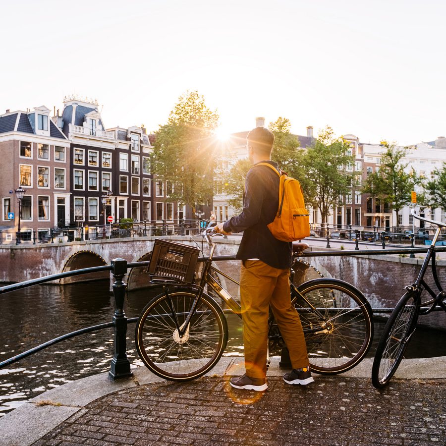 A man holds onto his bike as he looks out into the Amsterdam canals at sunset. 