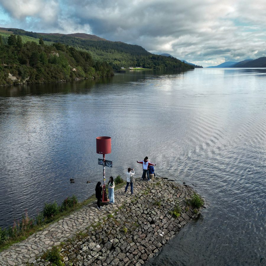 People posing for a photograph at the Loch Ness lake in the daytime. 