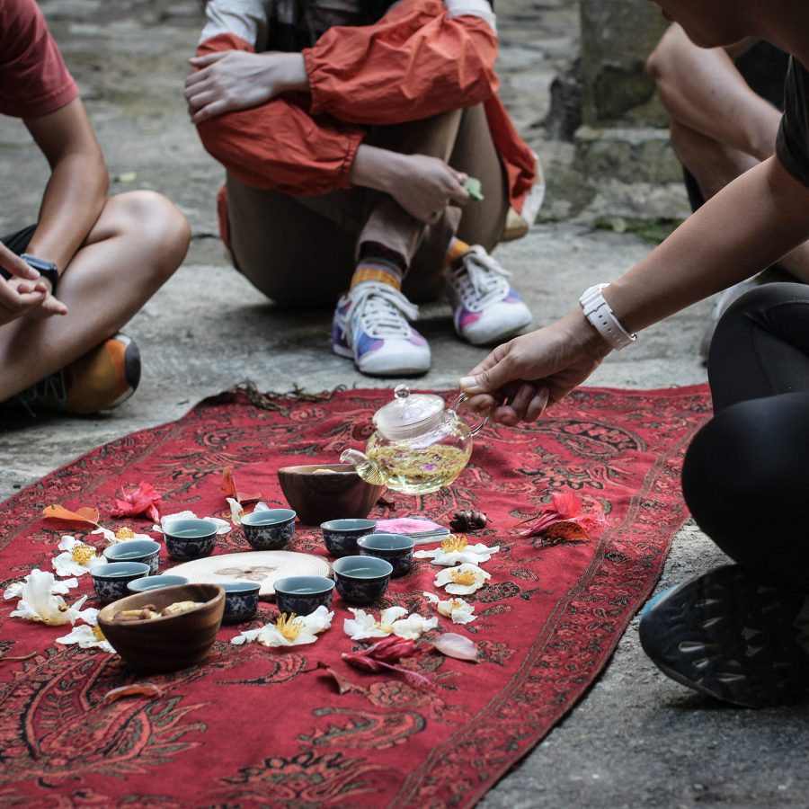 People inspecting items laid out on a red blanket.  