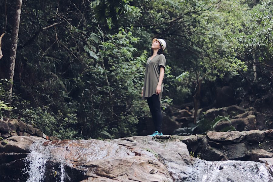 Woman stands on a rock in the middle of the forest staring at the sky.