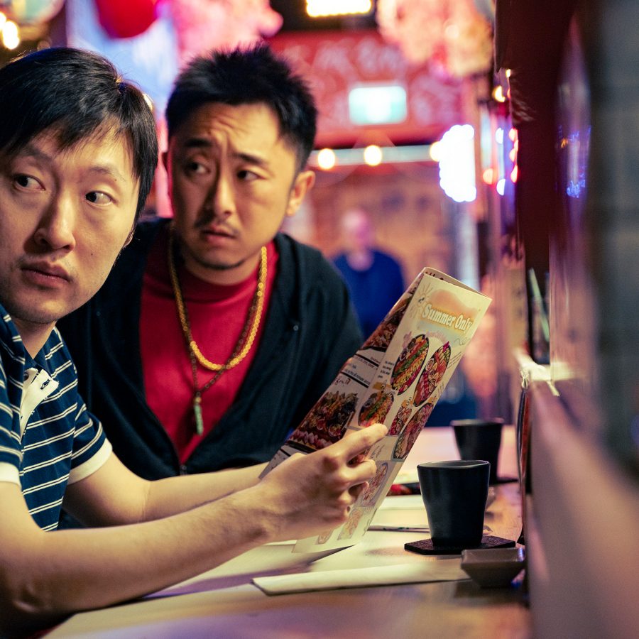 A scene from Fresh off Markham shows young man Shan (Nian Chang) sitting at a restaurant counter with a friend, looking nervous.  