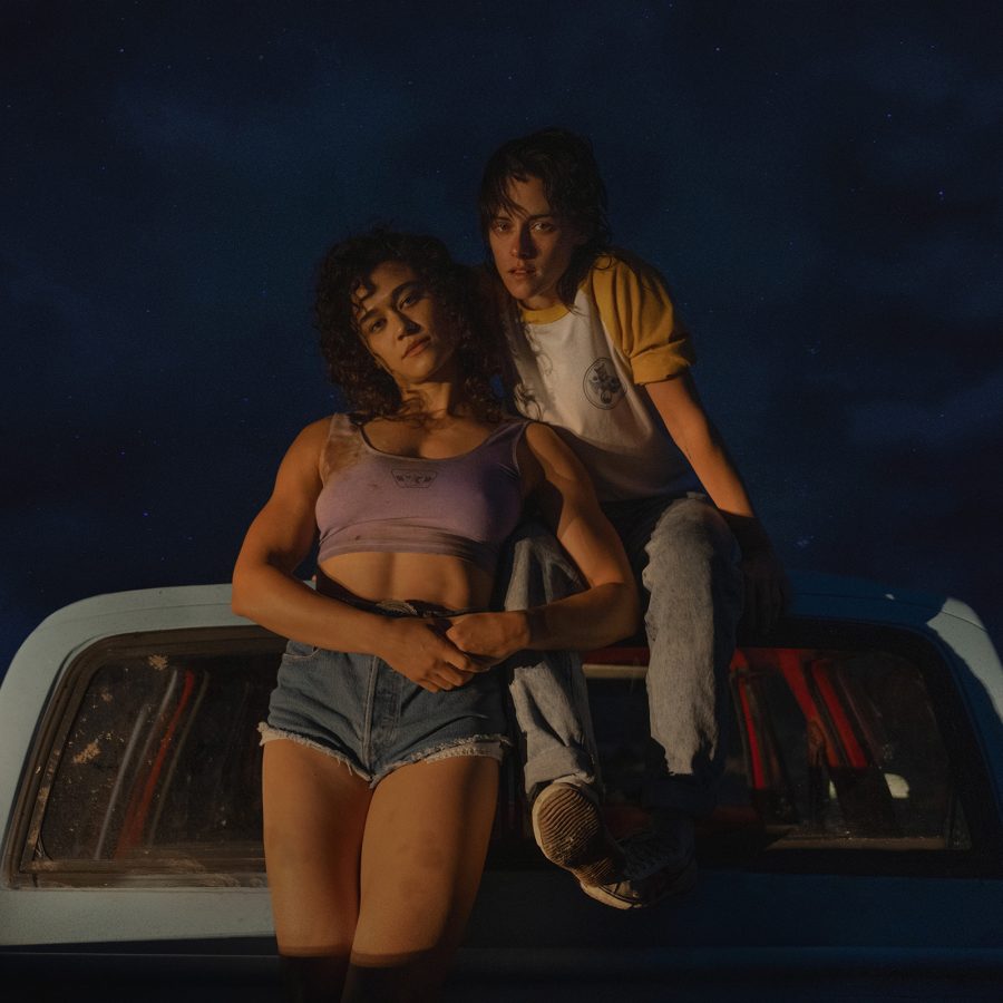  In an image from Love Lies Bleeding, the film’s two female protagonists – Lou (Kristen Stewart) and Jackie (Katy O’Brian) sit on the back of a pick-up truck at night.  