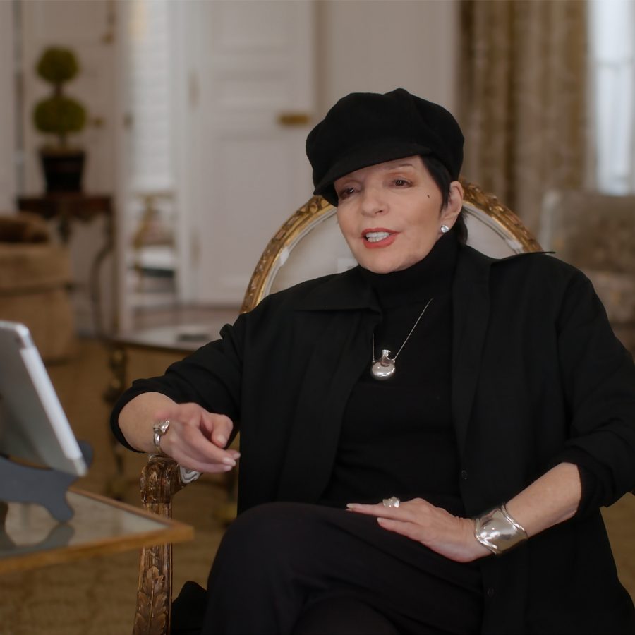 In a scene from Liza: A Truly Terrific Absolutely True Story, Liza Minnelli sits for an interview in a cream living room; she is dressed in black. 