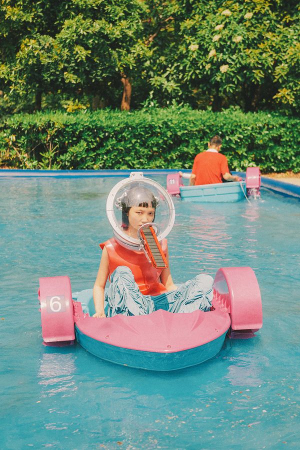 A woman sits in a small pink boat in a pool.